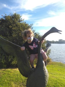 Little girl in a mask climbing on a statue of a swan.